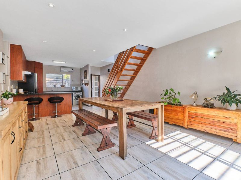 Open-plan living and dining area featuring tiled floors, a wooden staircase, and a functional kitchen with built-in cabinetry.