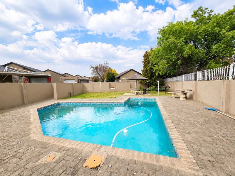 Private backyard featuring a swimming pool, paved patio area, and a small garden with a thatched lapa, enclosed by perimeter walls.
