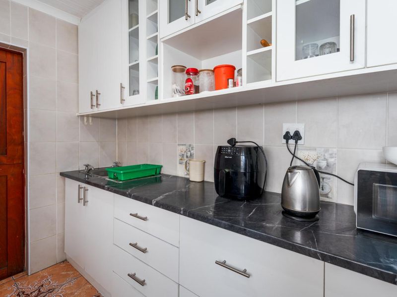 A functional scullery area featuring white cabinetry, dark laminate countertops, and tiled splashbacks, providing additional workspace and storage adjacent to the main kitchen.