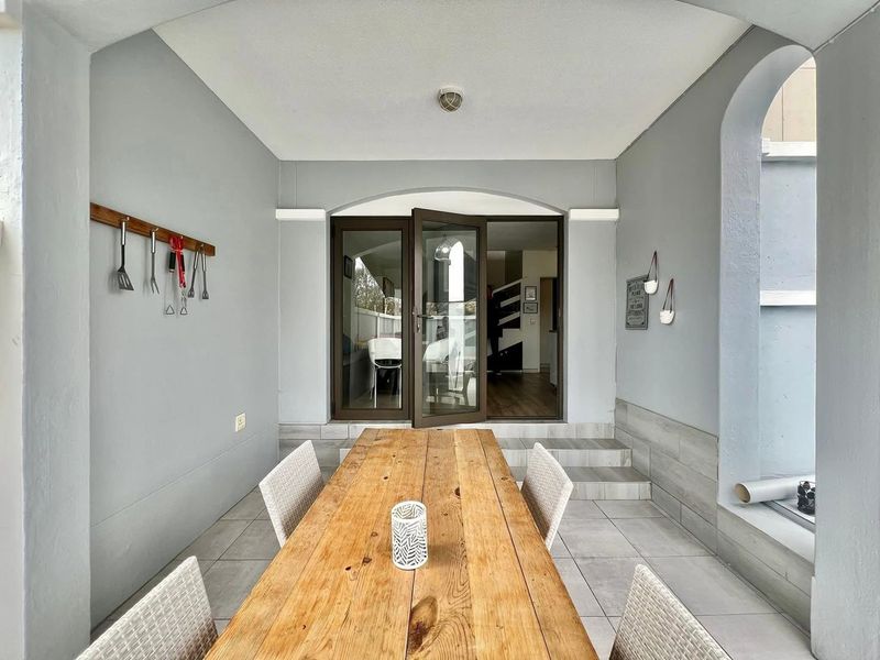 A covered patio area featuring tiled flooring, an arched architectural detail, and double french doors providing access to the interior living space.