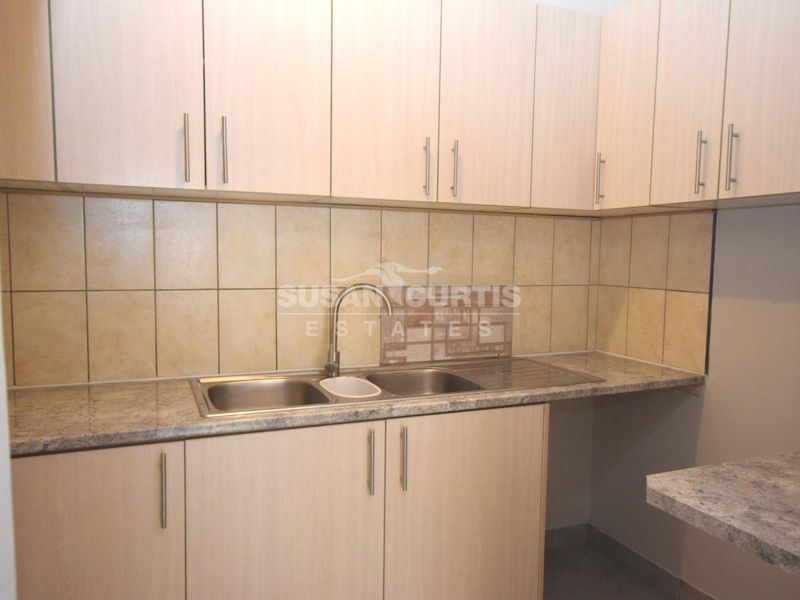 A functional kitchen area featuring light wood-tone cabinetry, stone-look laminate countertops, a double bowl stainless steel sink, and neutral ceramic tile backsplash.