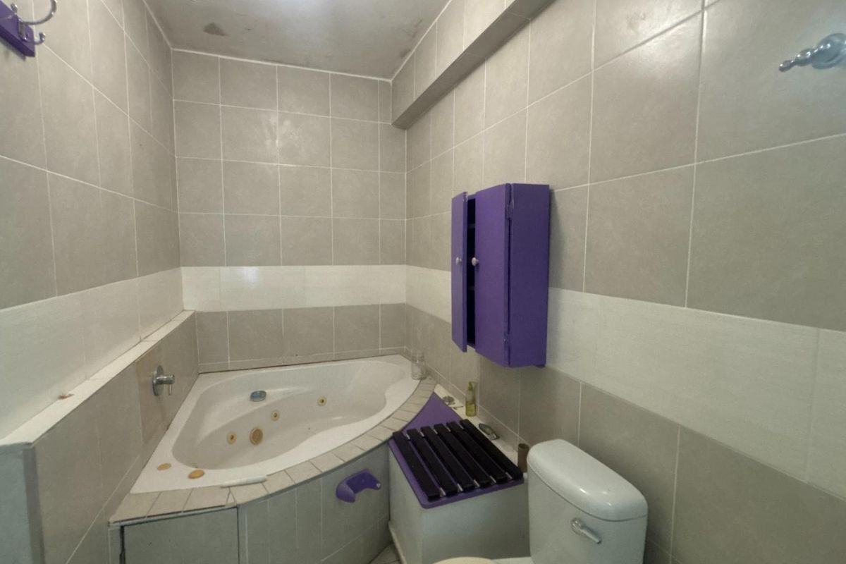 A bathroom featuring a corner spa bath, wall-mounted storage cabinet, and tiled walls. The space shows signs of ceiling water staining and dated finishes.