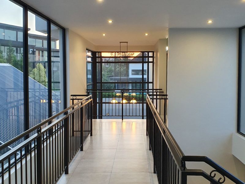 A bright and modern upper-level hallway featuring tiled flooring, sleek metal balustrades, and expansive windows providing natural light and views.