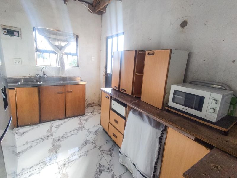 A dated kitchen featuring tiled flooring, built-in wooden cabinetry, and a stainless steel sink, requiring significant cosmetic updates and repairs to wall finishes.