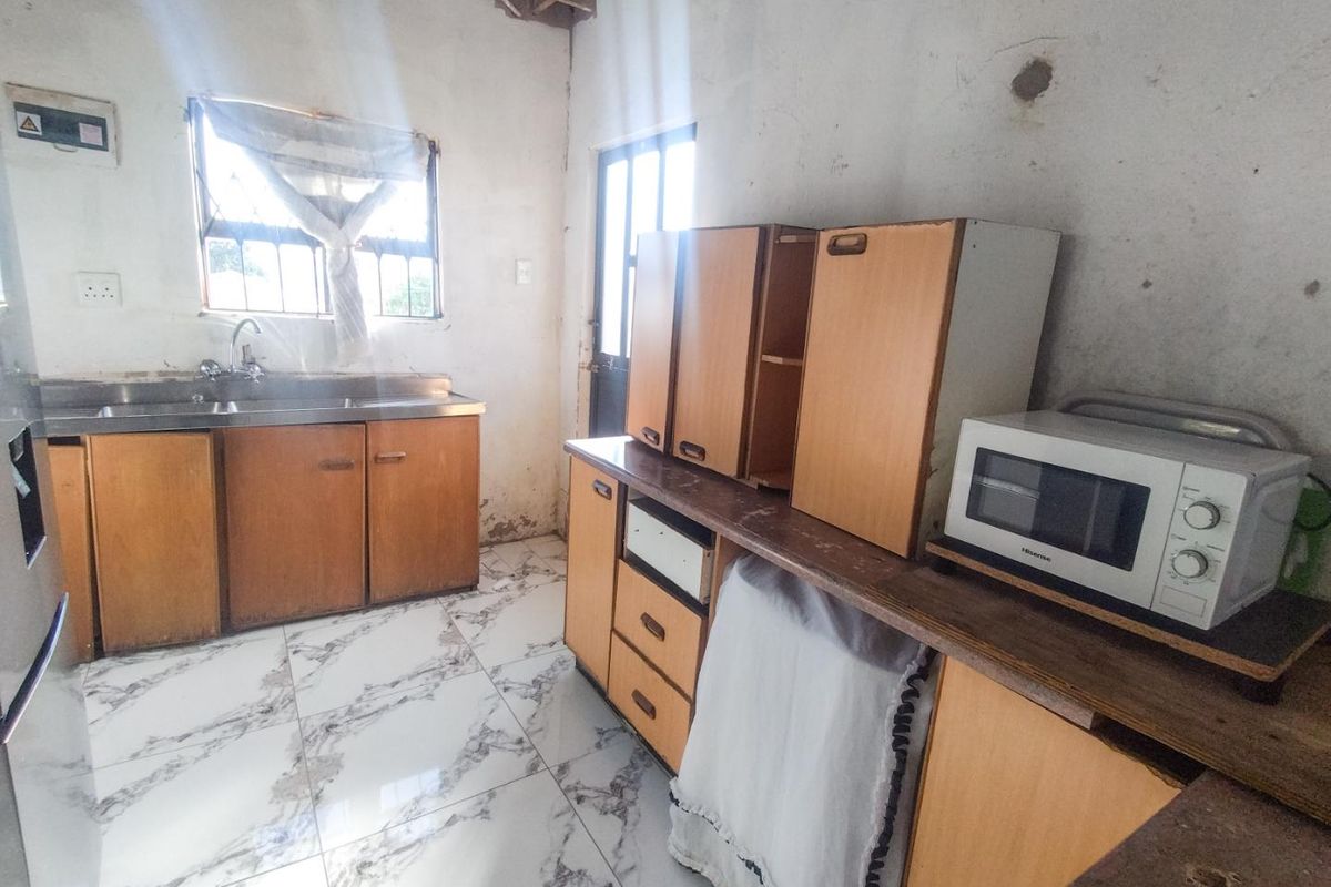 A dated kitchen featuring tiled flooring, built-in wooden cabinetry, and a stainless steel sink, requiring significant cosmetic updates and repairs to wall finishes.