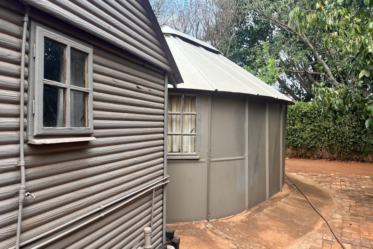 Exterior view of a unique circular structure with corrugated metal cladding and timber-framed windows, set within a garden area with brick paving.