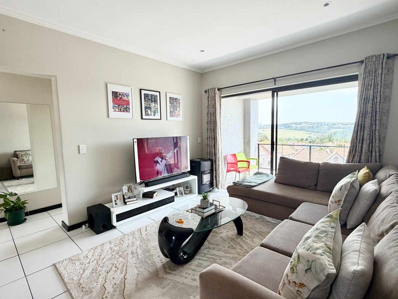 A bright living room featuring tiled flooring, recessed lighting, and a large sliding glass door that opens onto a balcony with scenic views.