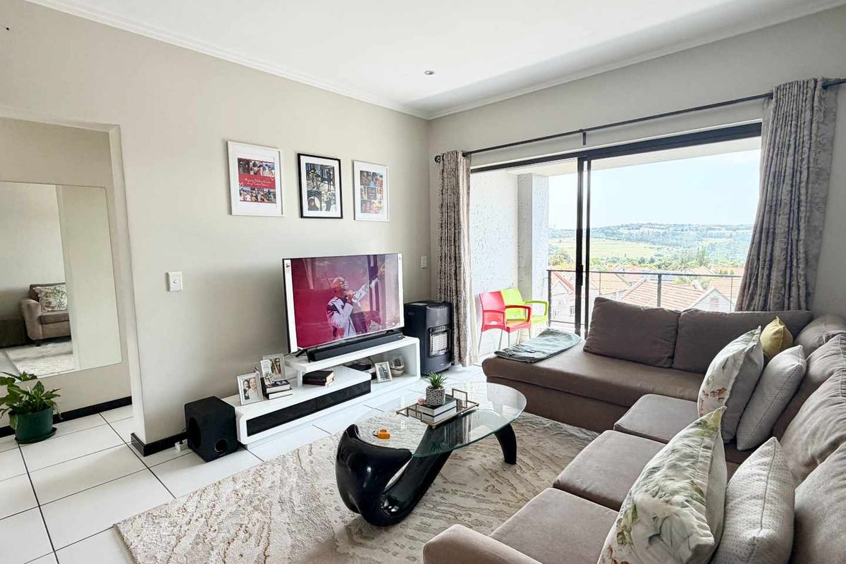 A bright living room featuring tiled flooring, recessed lighting, and a large sliding glass door that opens onto a balcony with scenic views.