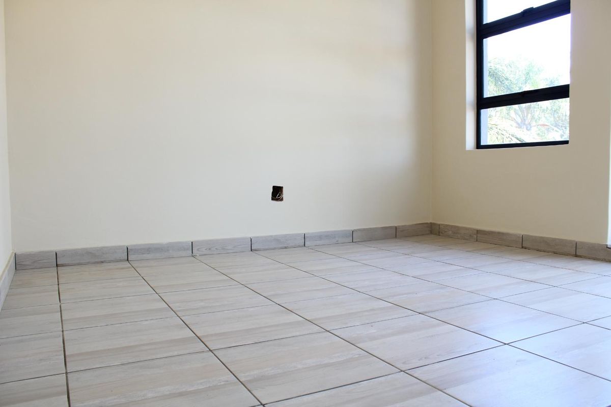 A bright, empty bedroom featuring neutral wood-look floor tiles, matching skirting, and a modern aluminium window frame.