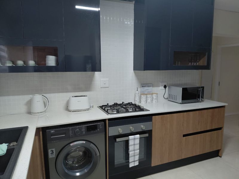 Modern kitchen featuring dark blue and wood-tone cabinetry, white quartz countertops, a gas hob, built-in oven, and a clean tiled backsplash.