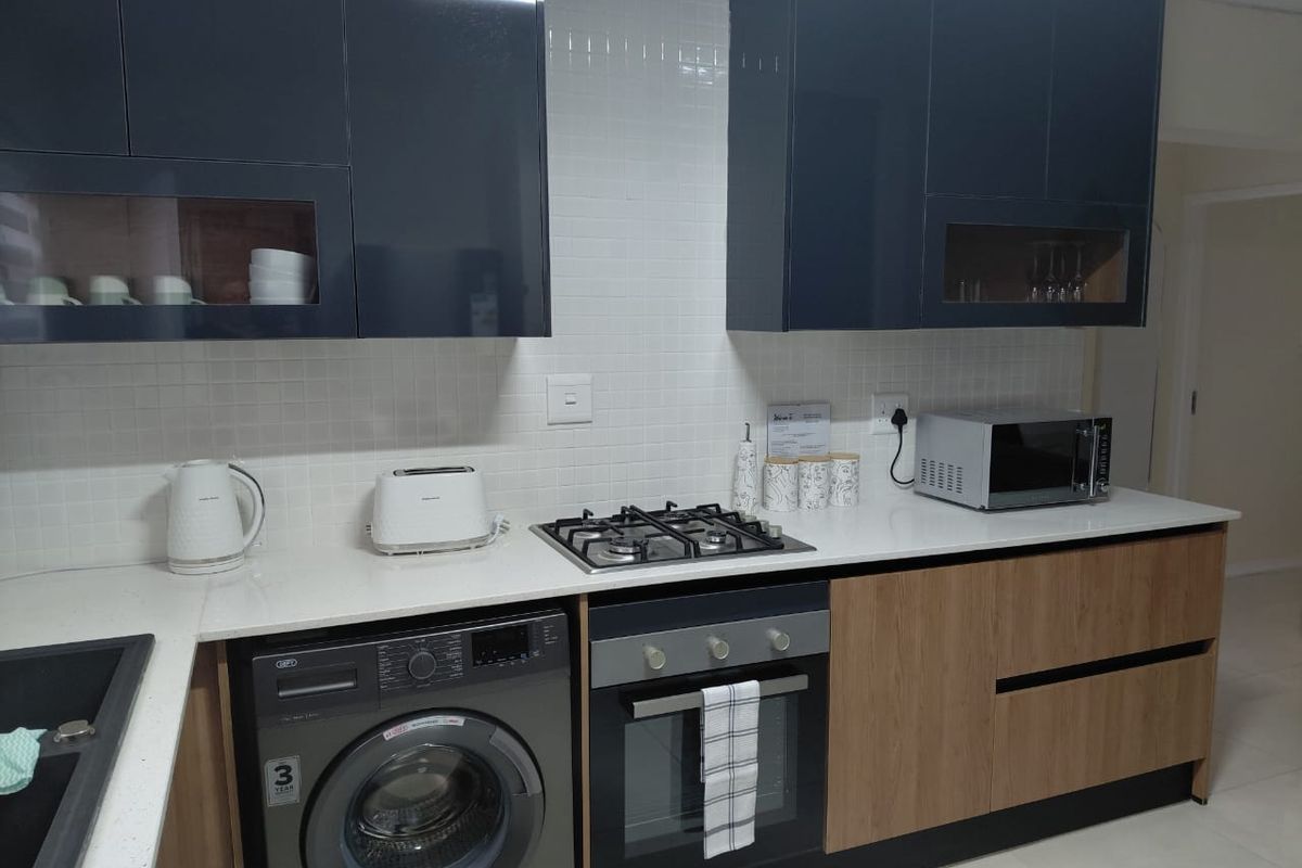 Modern kitchen featuring dark blue and wood-tone cabinetry, white quartz countertops, a gas hob, built-in oven, and a clean tiled backsplash.
