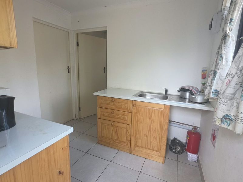 A functional kitchen area featuring pine cabinetry, laminate countertops, a stainless steel sink, and tiled flooring, offering potential for modernization.