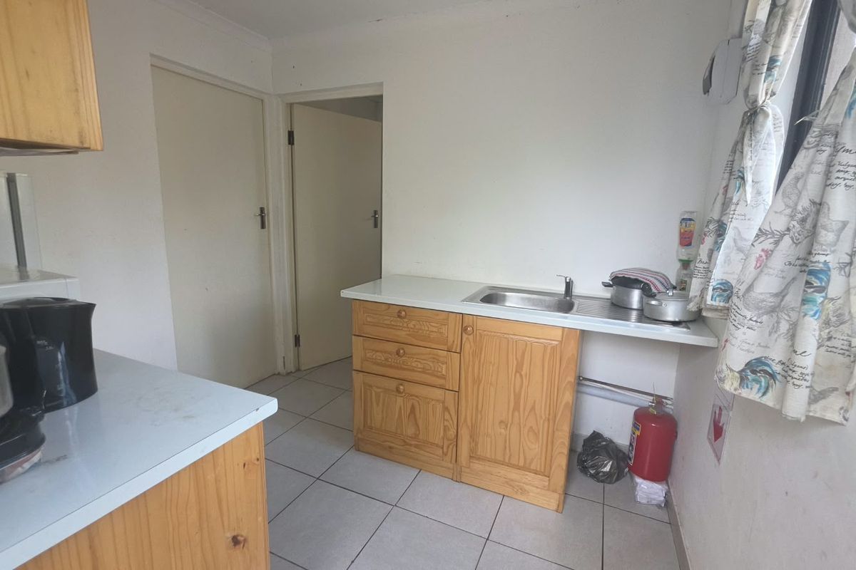 A functional kitchen area featuring pine cabinetry, laminate countertops, a stainless steel sink, and tiled flooring, offering potential for modernization.