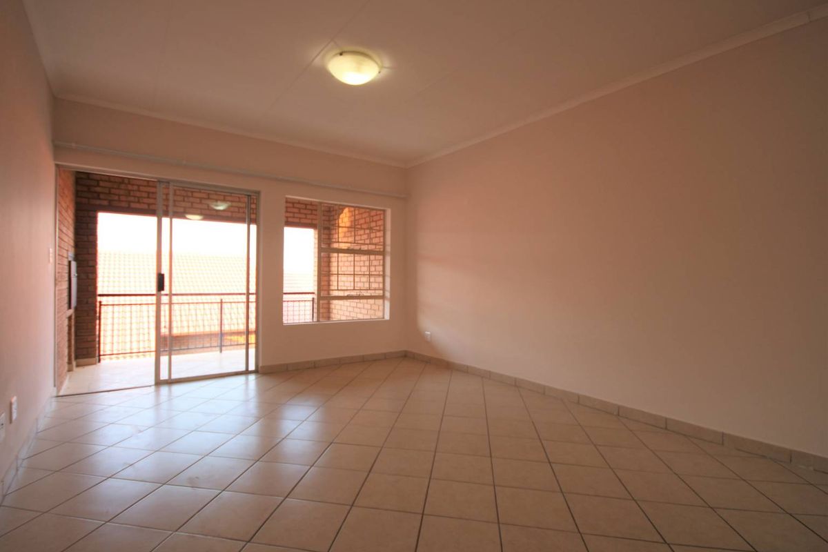 A spacious, empty living area featuring neutral tiled flooring, large windows, and a sliding glass door leading to an outdoor balcony.