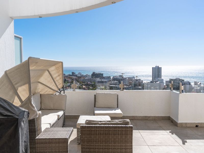 Spacious balcony featuring a glass balustrade and tiled flooring, offering expansive coastal and city views.