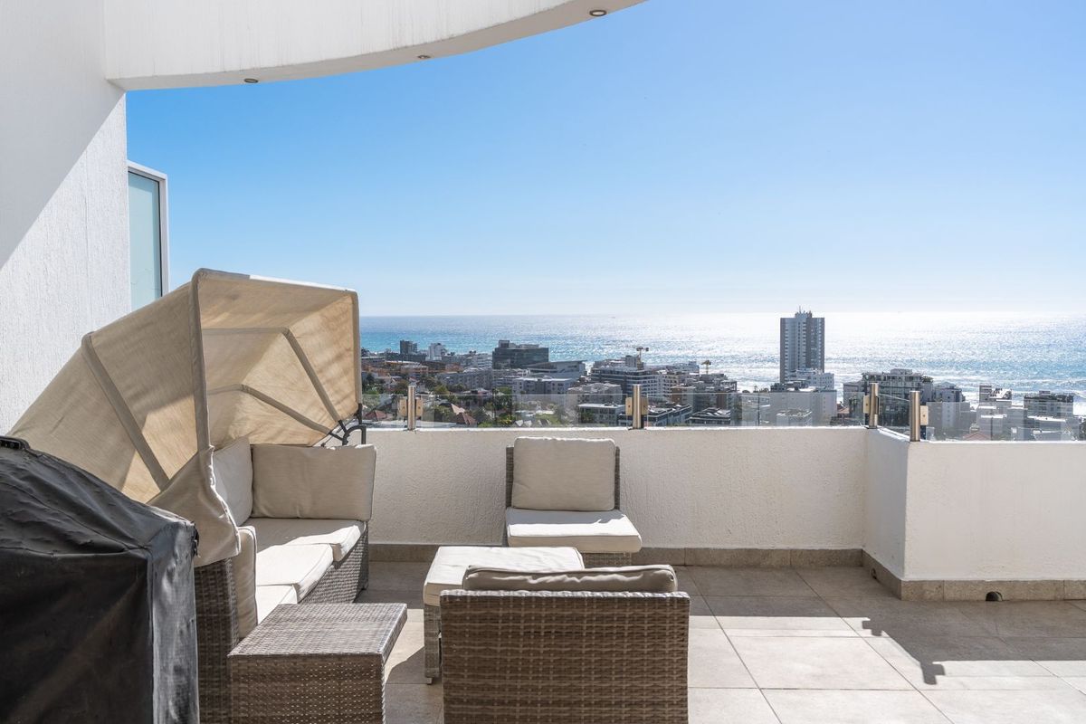 Spacious balcony featuring a glass balustrade and tiled flooring, offering expansive coastal and city views.