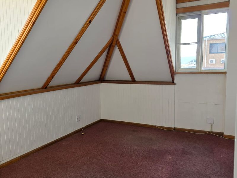 An empty attic-style bedroom featuring exposed timber rafters, timber wall paneling, and a single window, offering a blank canvas for renovation.