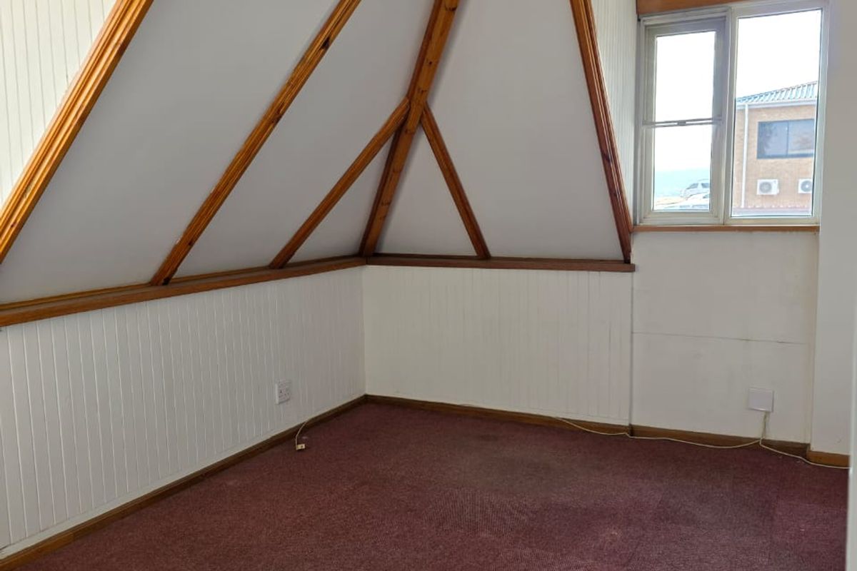 An empty attic-style bedroom featuring exposed timber rafters, timber wall paneling, and a single window, offering a blank canvas for renovation.