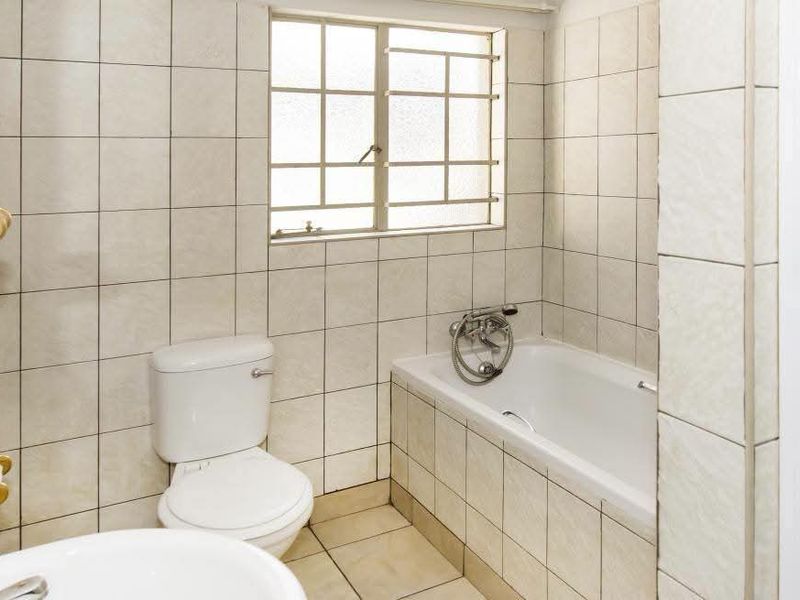 A functional bathroom featuring a bathtub, toilet, and basin with neutral wall and floor tiling, offering a clean and practical layout.