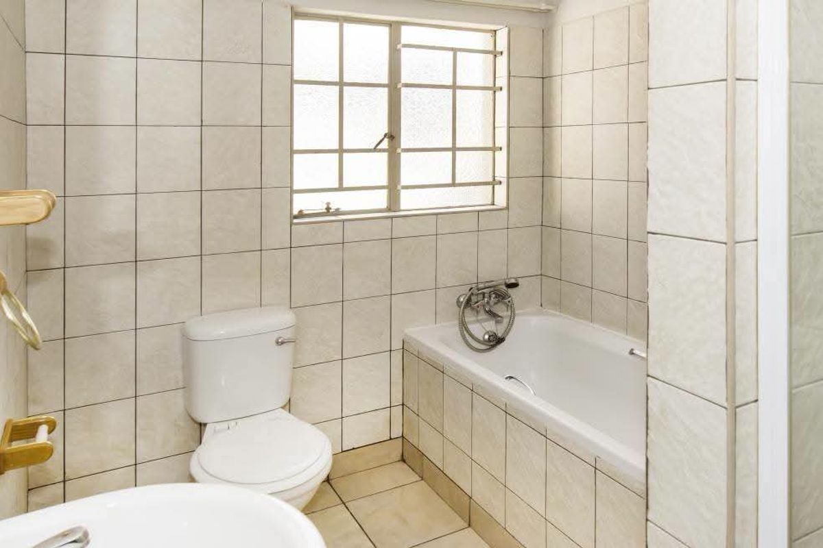 A functional bathroom featuring a bathtub, toilet, and basin with neutral wall and floor tiling, offering a clean and practical layout.
