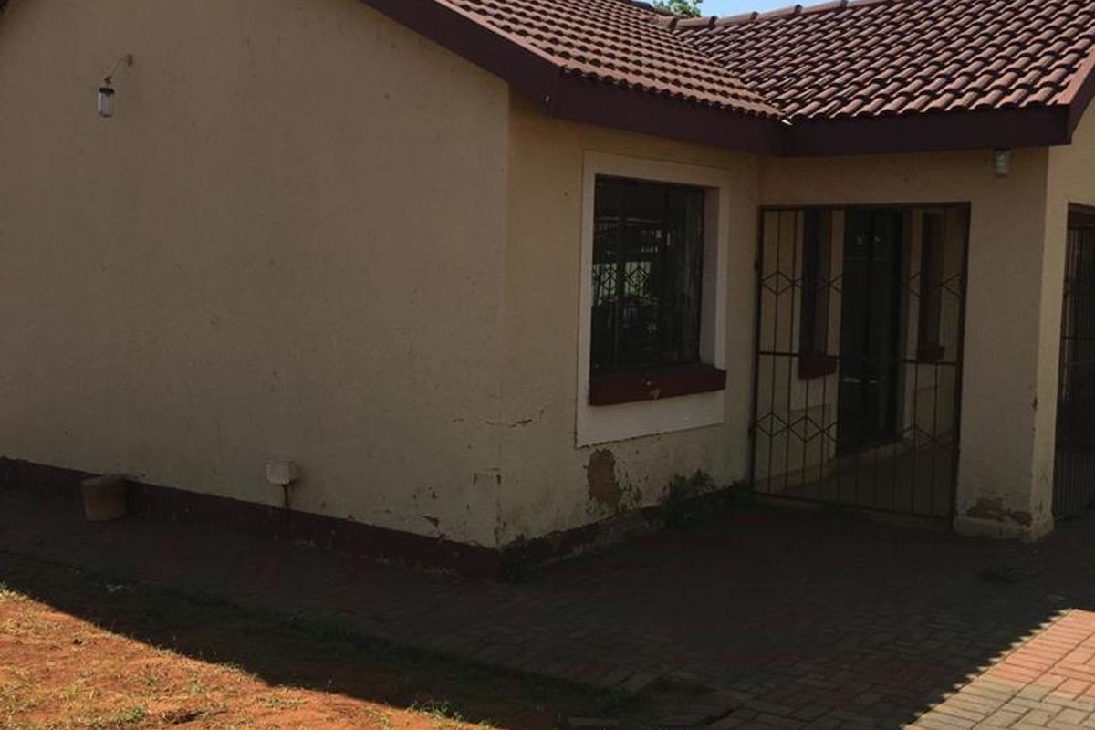 Rear view of the property featuring a tiled roof, paved walkway, and security gate, showing signs of exterior wall wear and paint deterioration.