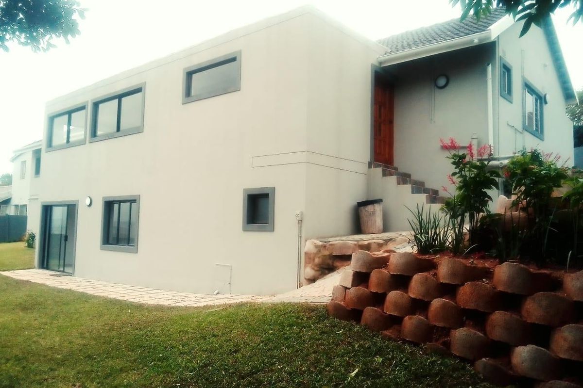 Rear view of a multi-level house featuring a paved walkway, retaining wall, and external staircase leading to the entrance.