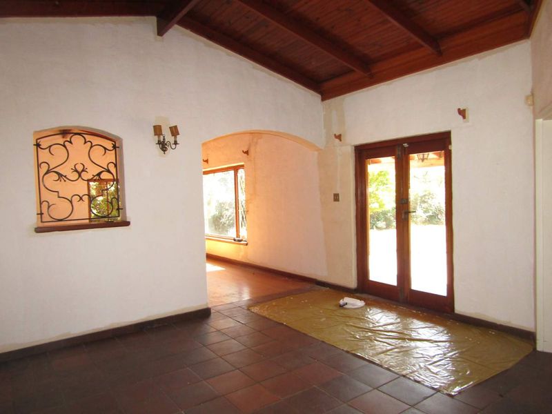 Spacious living area featuring exposed timber ceilings, terracotta flooring, and an arched transition to an adjacent room, currently undergoing interior maintenance.
