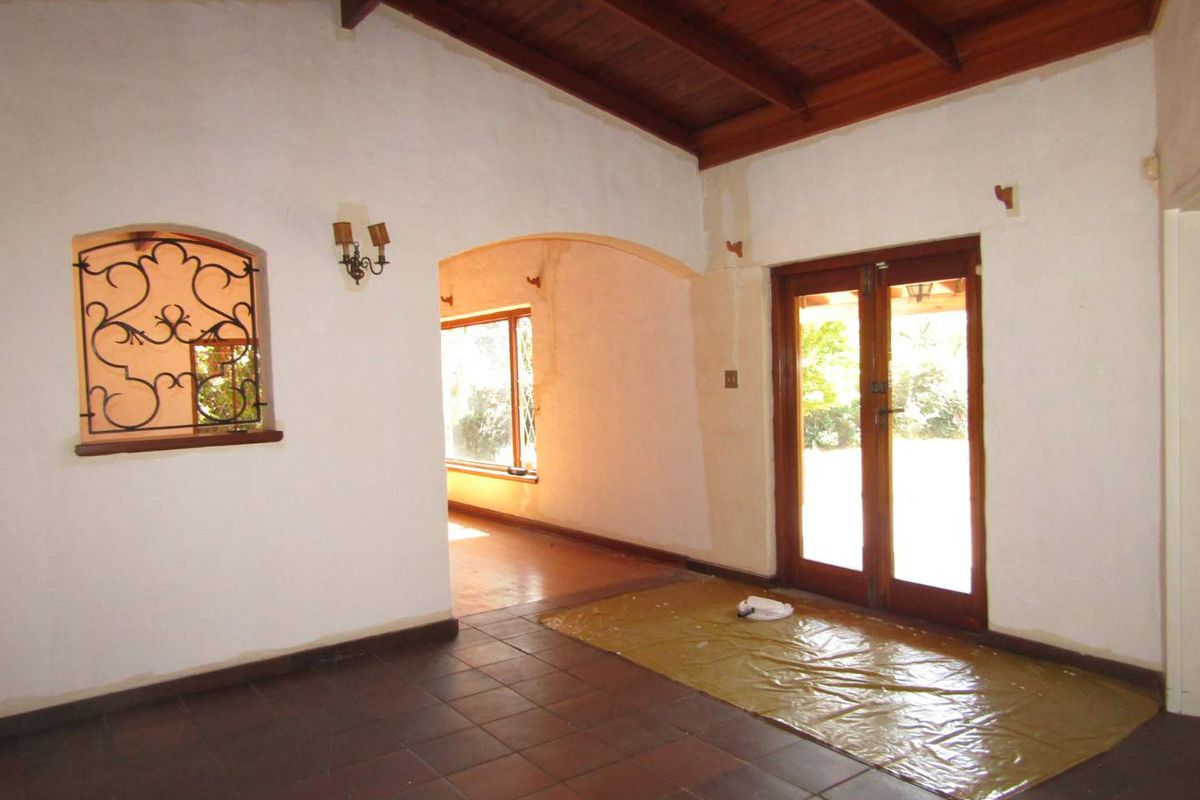 Spacious living area featuring exposed timber ceilings, terracotta flooring, and an arched transition to an adjacent room, currently undergoing interior maintenance.
