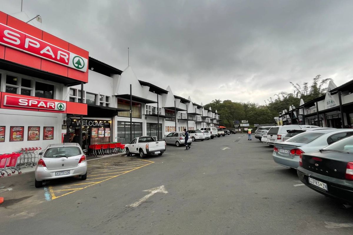 Exterior view of a retail shopping center featuring a SPAR storefront, paved parking area, and covered walkways.