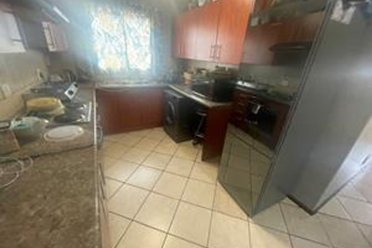 A functional kitchen featuring built-in wooden cabinetry, laminate countertops, a hob, and an integrated oven, with tiled flooring throughout.