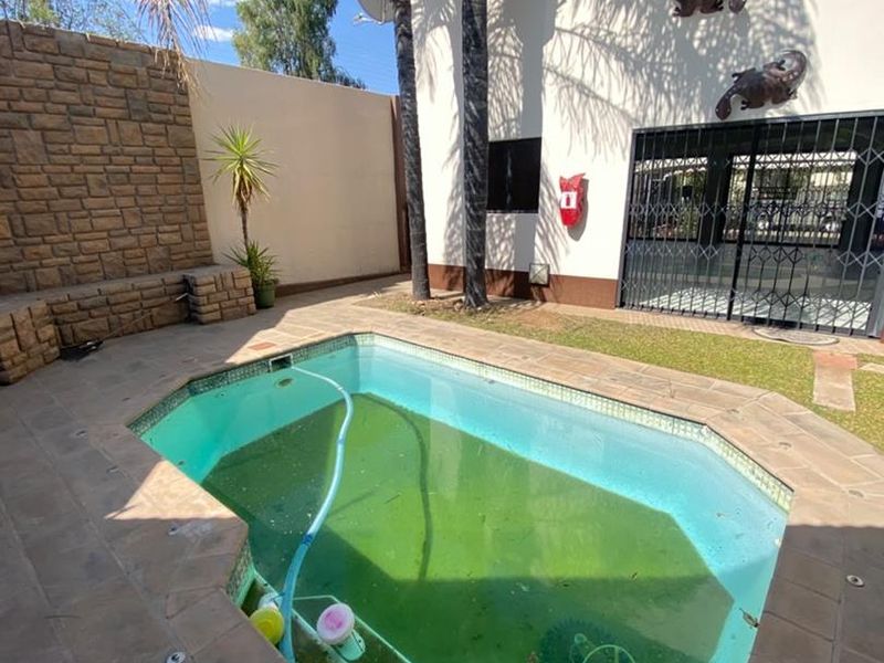 Outdoor pool area featuring a paved deck, stone feature wall, and security gate access. The pool requires professional cleaning and maintenance.