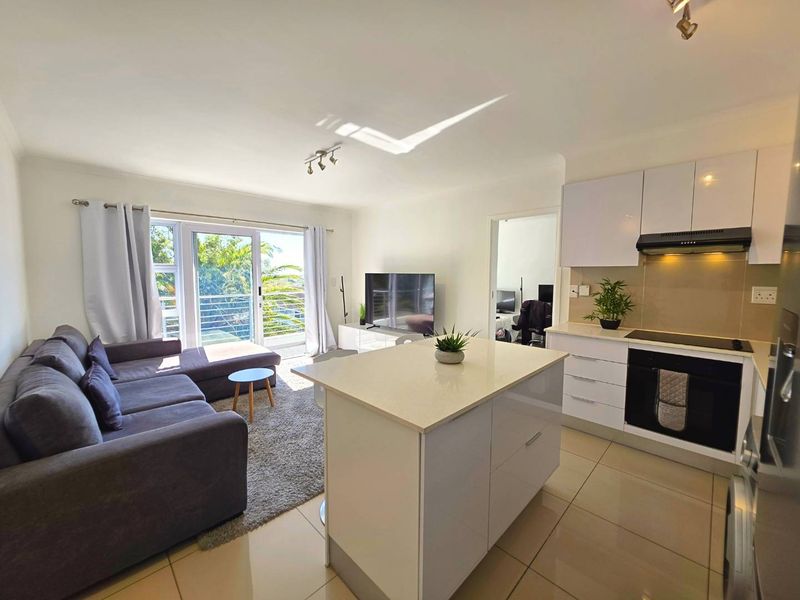 Modern open-plan living area featuring a sleek kitchen with a central island, built-in appliances, and direct access to a balcony through sliding glass doors.