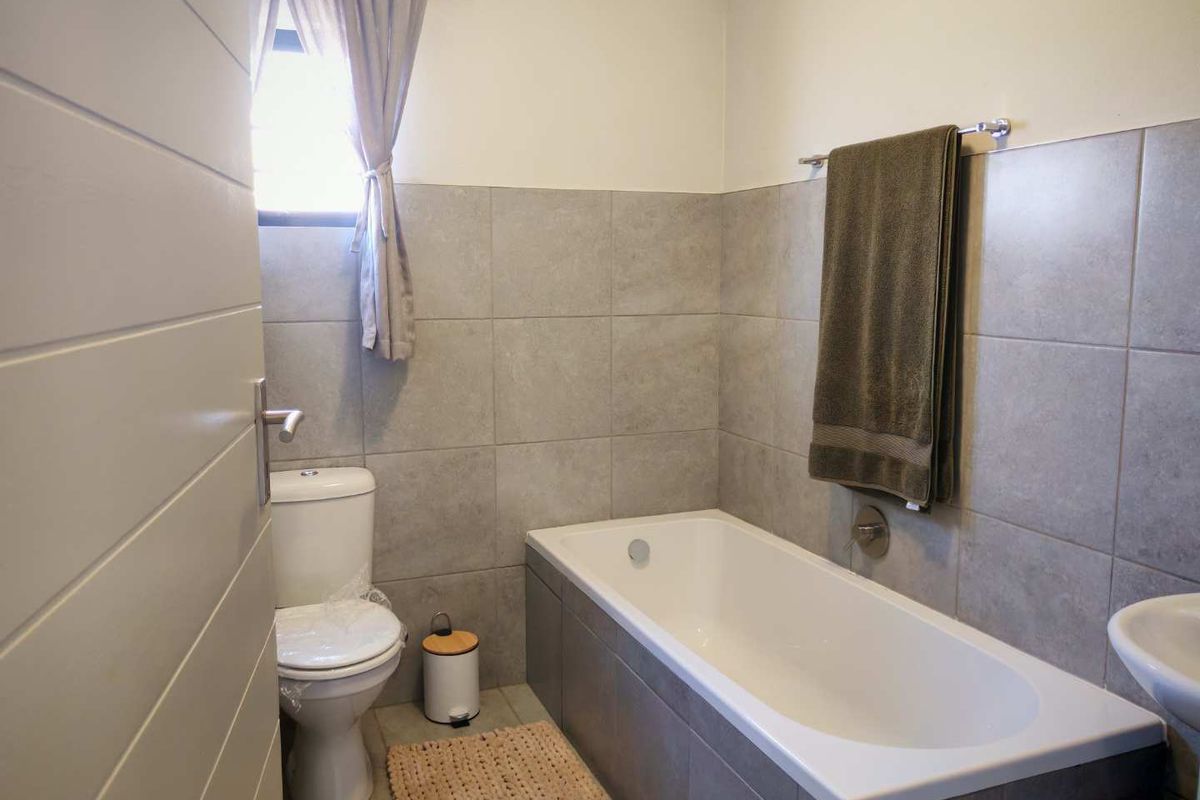 A functional bathroom featuring a built-in bathtub, a standard toilet, and neutral grey wall tiling.