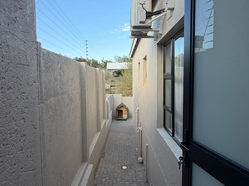 A narrow paved side passage featuring a boundary wall, tiled steps, and an external air conditioning unit.