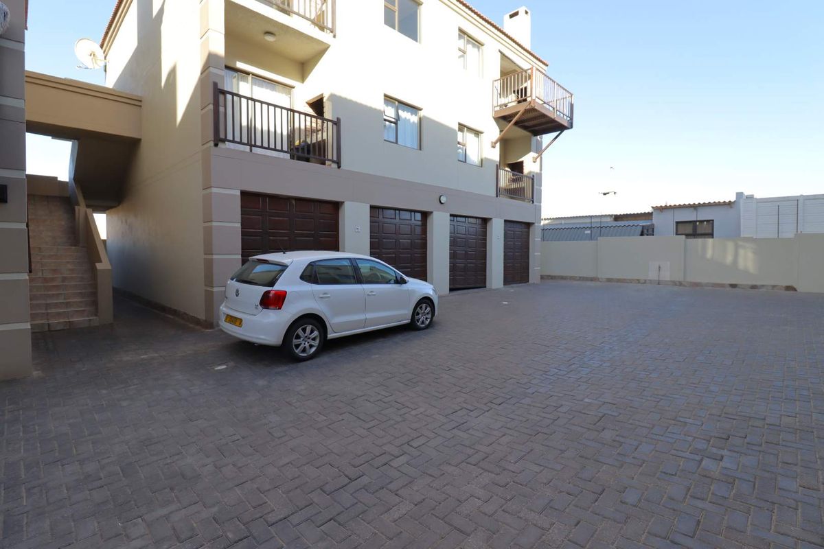 Exterior view of the apartment building featuring a paved parking area, multiple garage doors, and private balconies on the upper levels.