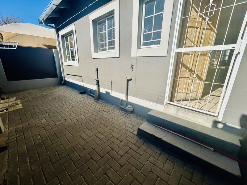 A paved rear courtyard area featuring a security gate, external water tap, and access to the building's rear entrance.