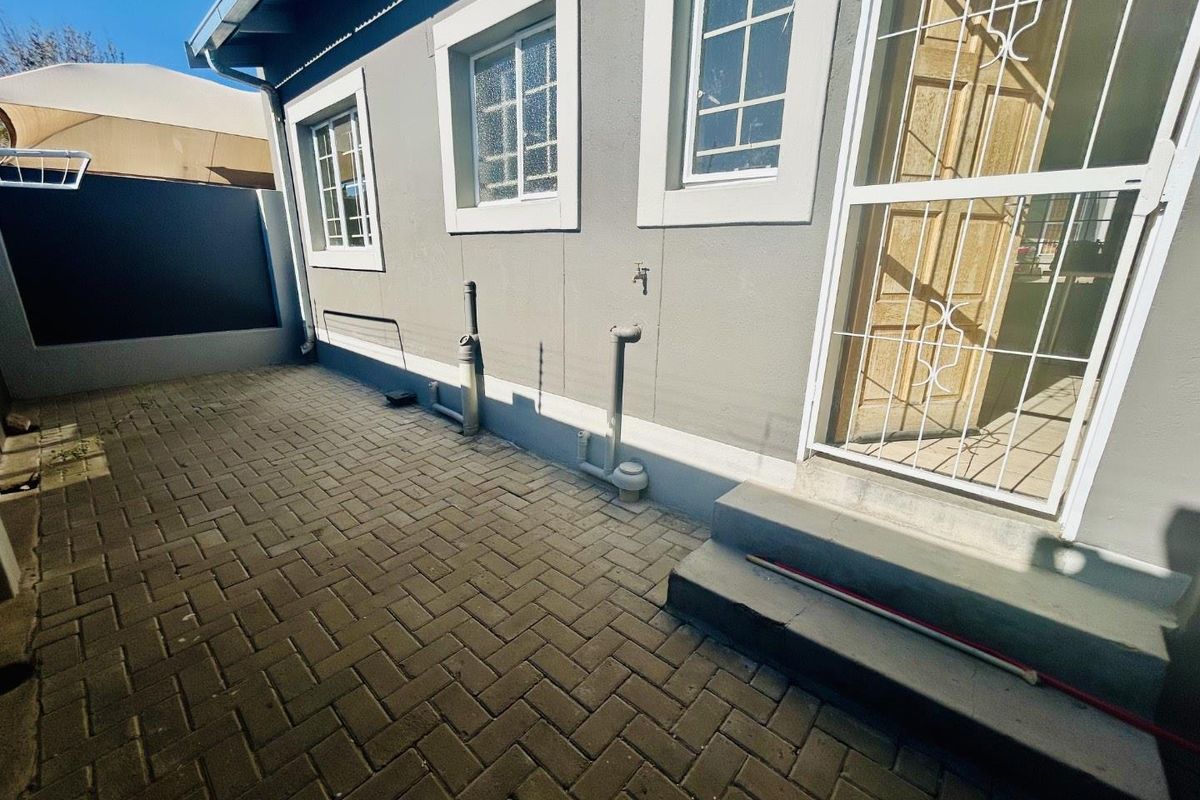 A paved rear courtyard area featuring a security gate, external water tap, and access to the building's rear entrance.