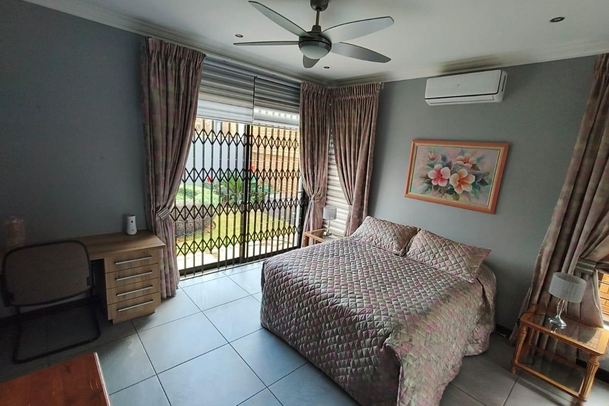 A well-maintained bedroom featuring tiled flooring, a ceiling fan, split-system air conditioning, and direct access to the garden through a secure sliding door.