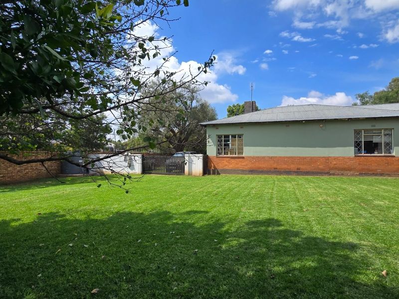 A spacious rear garden featuring a well-maintained lawn, brick boundary walls, and a view of the rear building elevation with a metal roof.