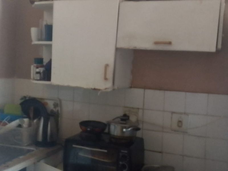 A compact kitchen area featuring basic cabinetry, a tiled backsplash, and a stainless steel sink, currently showing signs of wear and dated finishes.