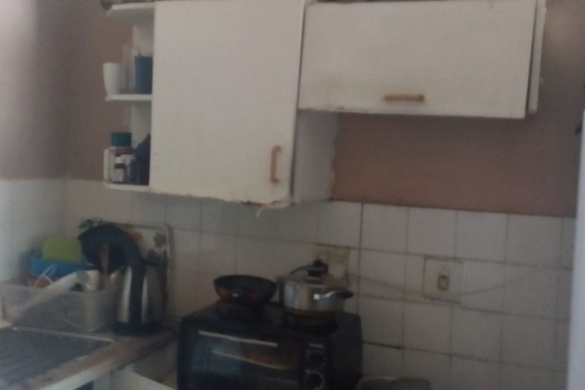 A compact kitchen area featuring basic cabinetry, a tiled backsplash, and a stainless steel sink, currently showing signs of wear and dated finishes.