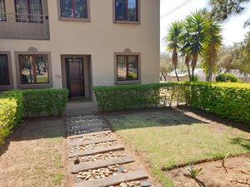 Front view of the apartment building featuring a paved walkway, manicured hedges, and a small garden area leading to the main entrance.