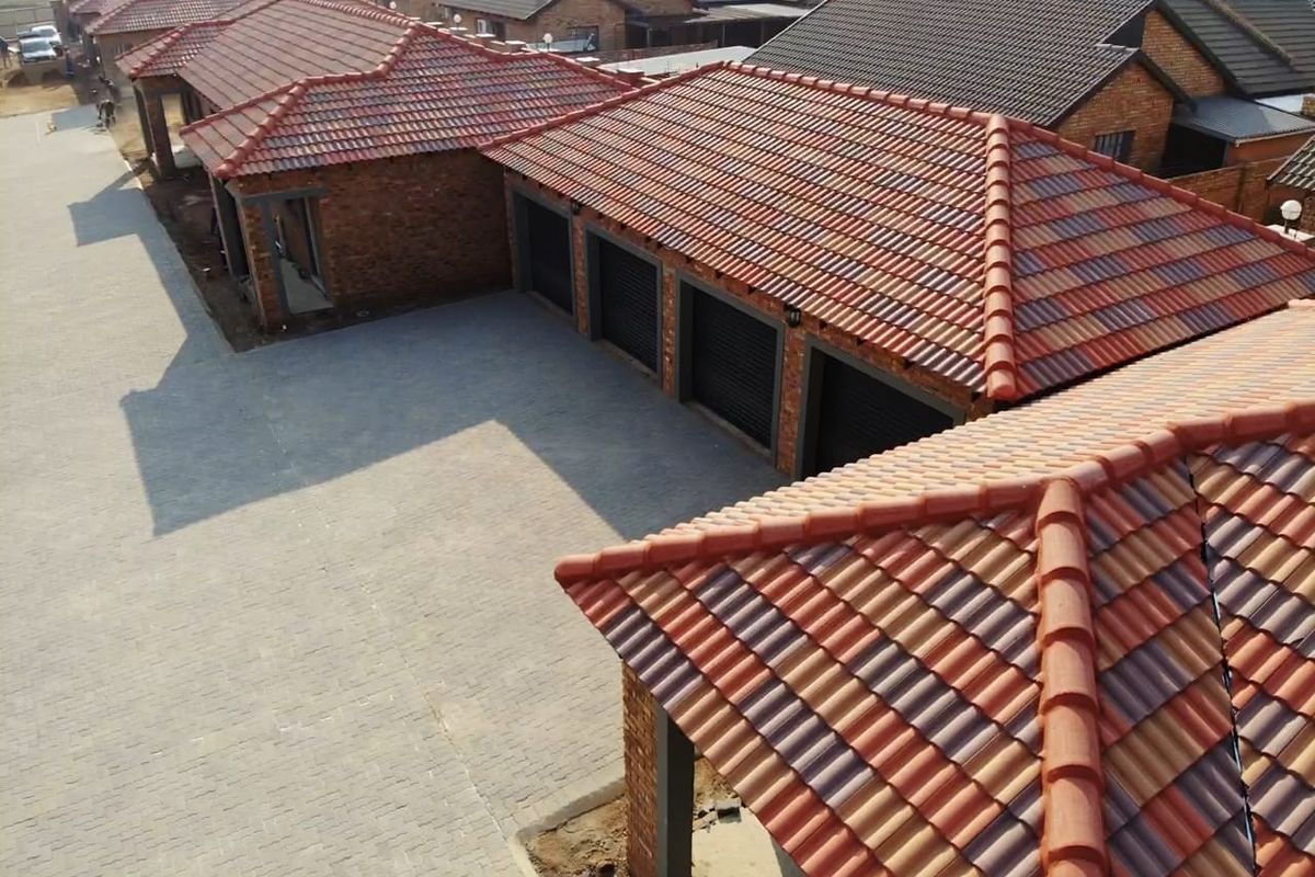 Aerial view of a townhouse complex featuring brick facades, terracotta tiled roofs, and paved driveway access to multiple garages.