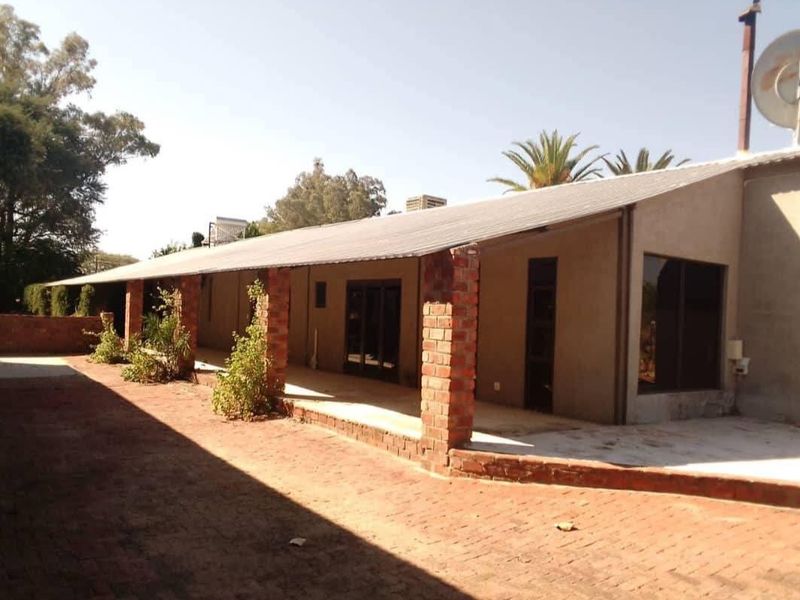 A spacious covered patio area featuring brick pillars and paved flooring, providing a functional outdoor entertainment space overlooking the property grounds.