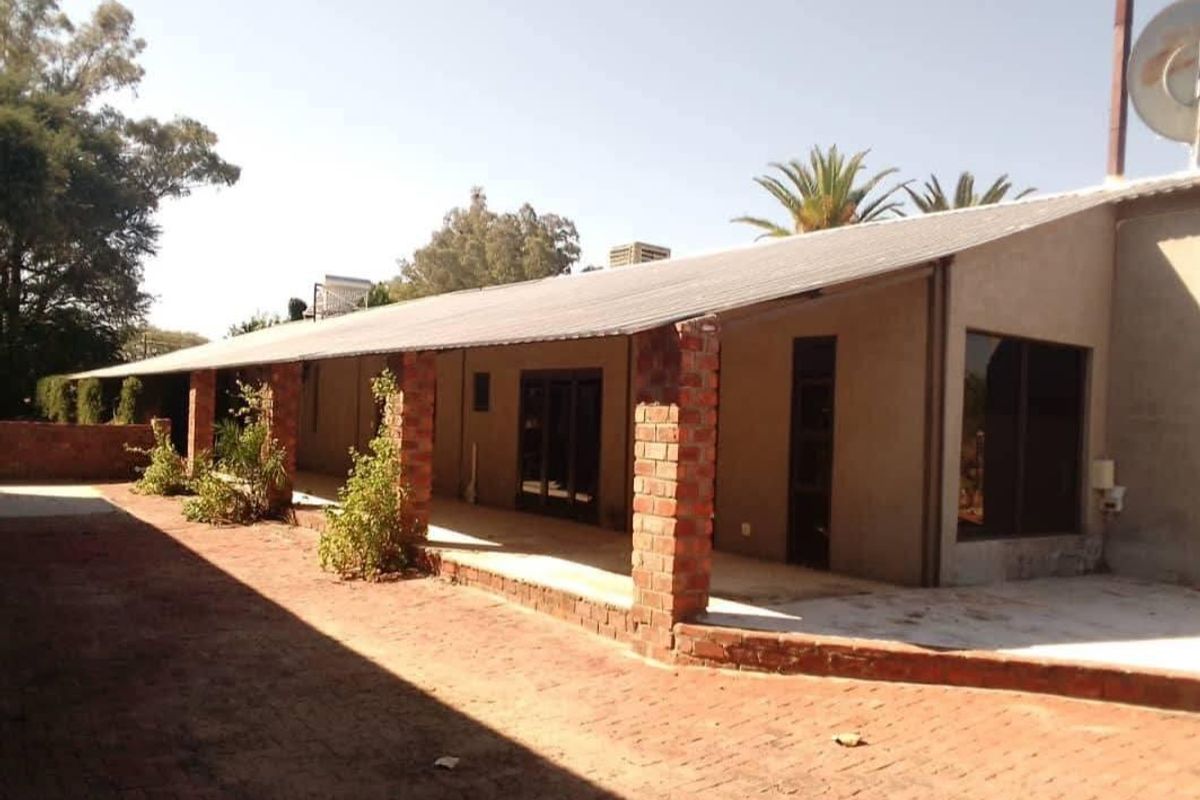 A spacious covered patio area featuring brick pillars and paved flooring, providing a functional outdoor entertainment space overlooking the property grounds.