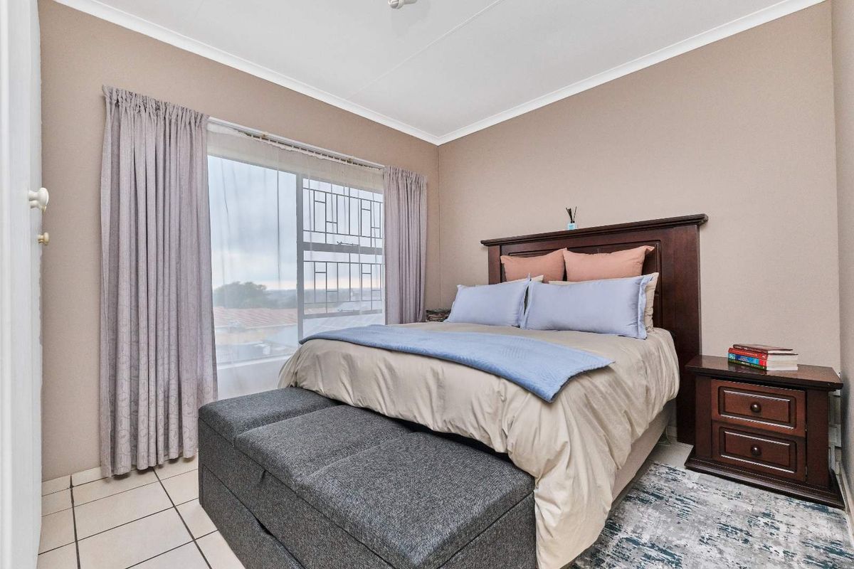 A well-lit bedroom featuring tiled flooring, large window with security bars, and neutral wall tones, providing a comfortable and functional living space.