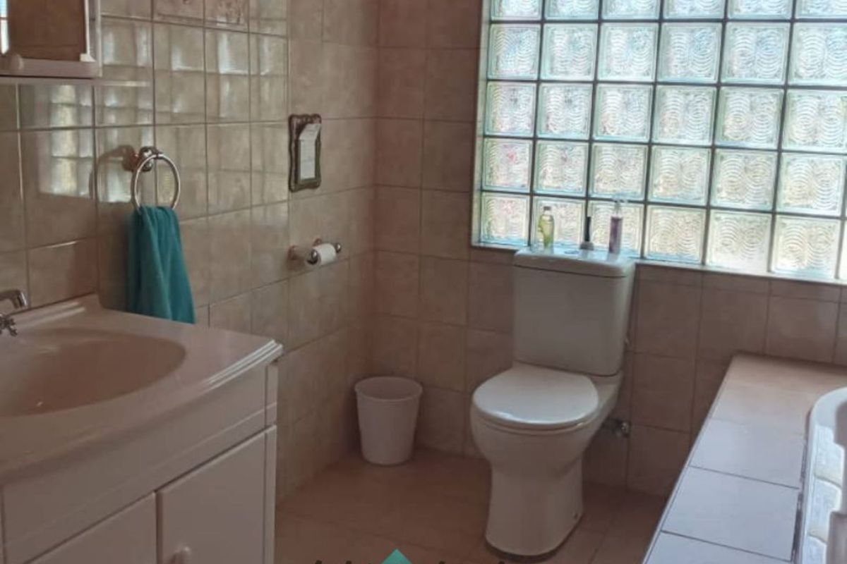 A functional bathroom featuring a vanity unit, toilet, and a tiled bathtub area with a glass block window for natural light.