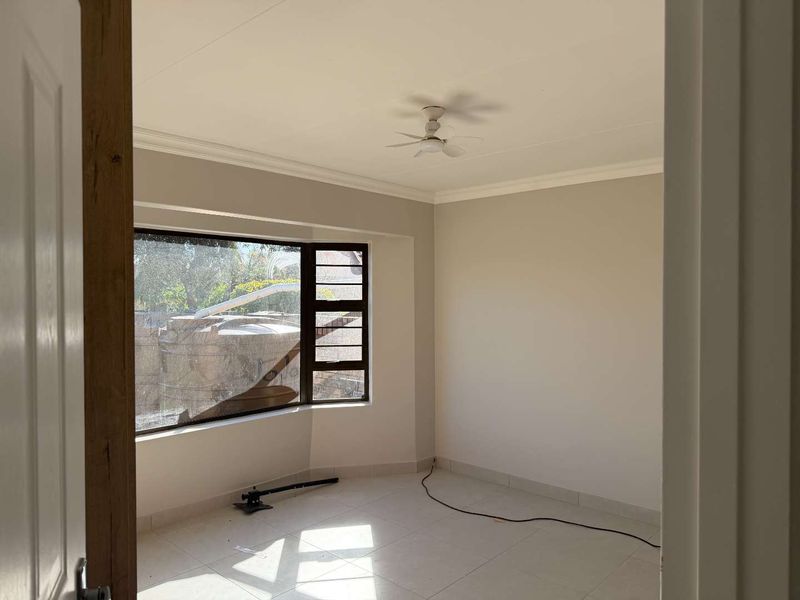 A bright, empty bedroom featuring tiled flooring, a ceiling fan, and a large bay window that allows for ample natural light.