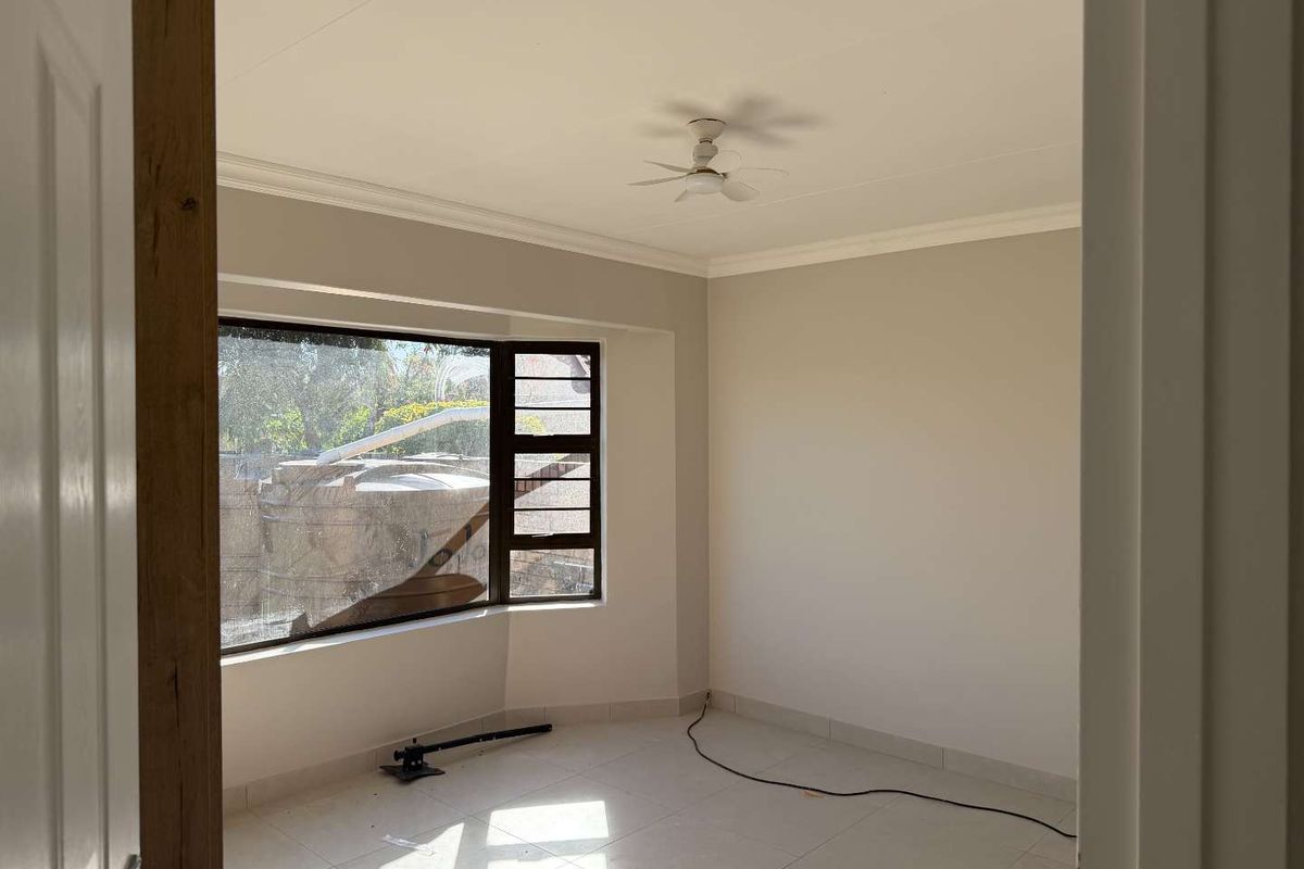A bright, empty bedroom featuring tiled flooring, a ceiling fan, and a large bay window that allows for ample natural light.