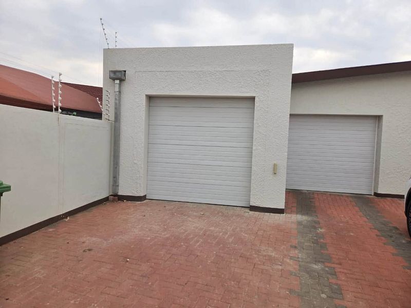 A view of a double garage with white sectional doors and a paved driveway, secured by perimeter boundary walls and electric fencing.